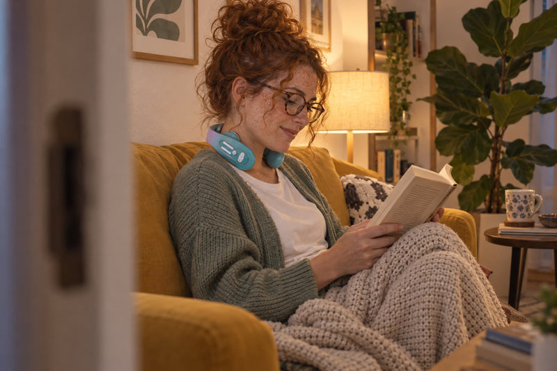 Chica pelirroja leyendo en un sofá con el masajeador cervical puesto